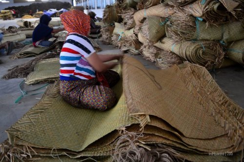 seorang pekerja yang menjahit tikar dengan tali rami supaya lebih lebar